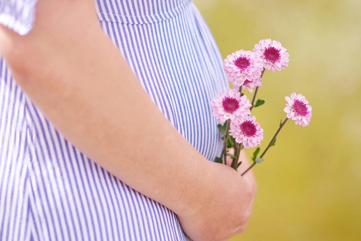 photo of lower half of a pregnant woman holding flowers