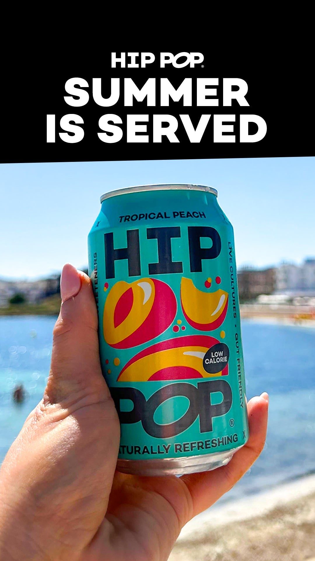 Hand holding a can of Hip Pop tropical peach soda against a sunny beach backdrop, with bold text reading “Summer is Served” above