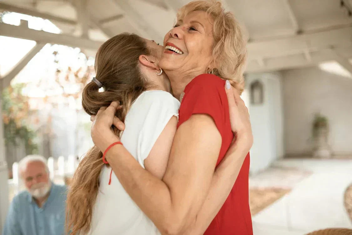 Mother and daughter hugging joyfully on Mother’s Day, with a man smiling in the background; a heartwarming moment perfect for celebrating Mother’s Day in the UK.