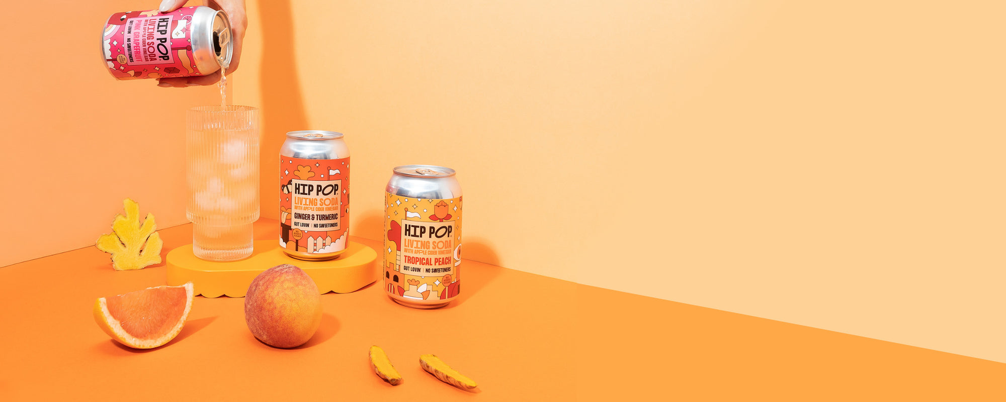 Hip Pop Living Soda collection with fruit and a hand picking up one of the cans and pour into a glass