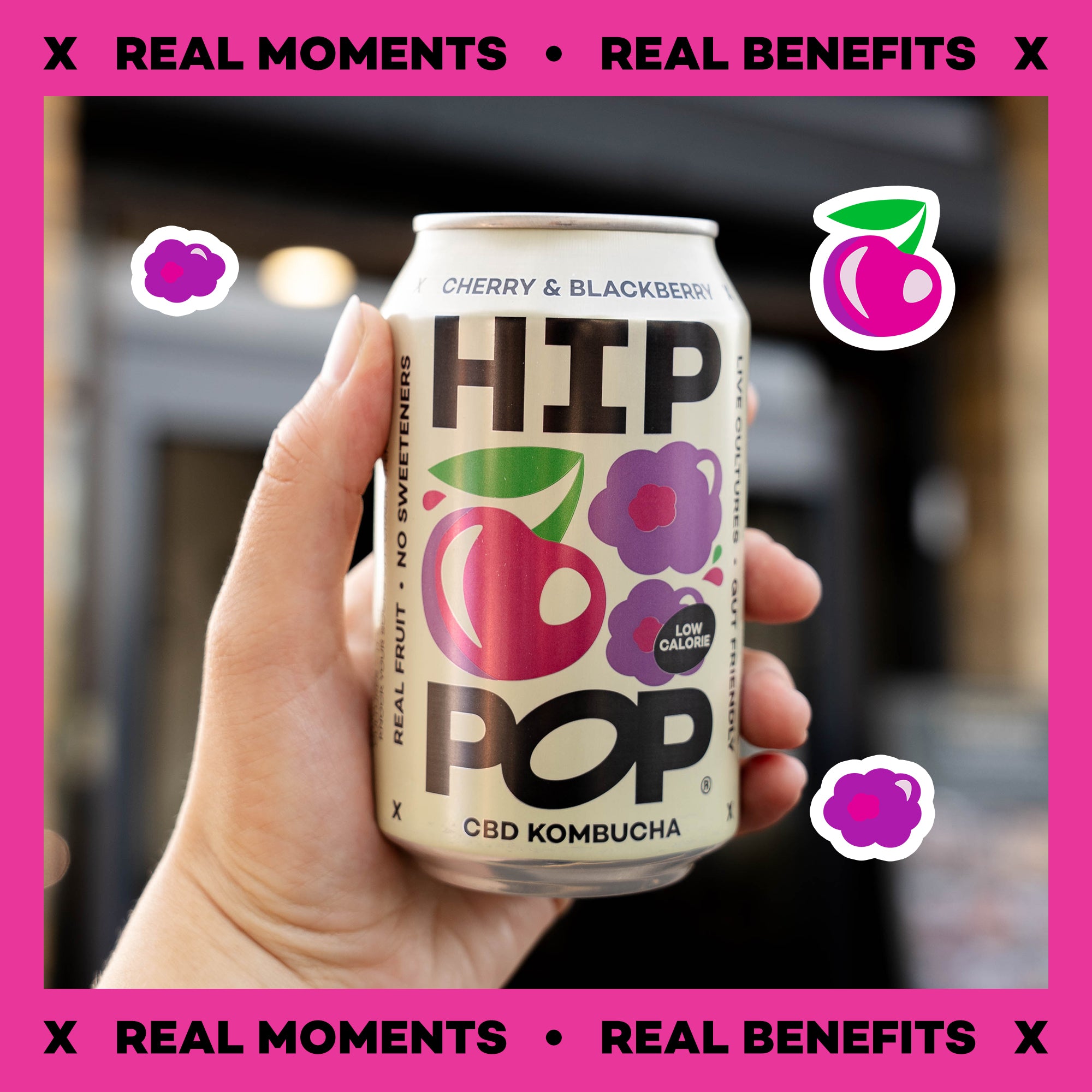 Hand holding a can of HIP POP CBD Kombucha with cherry and blackberry flavor against a pink background.