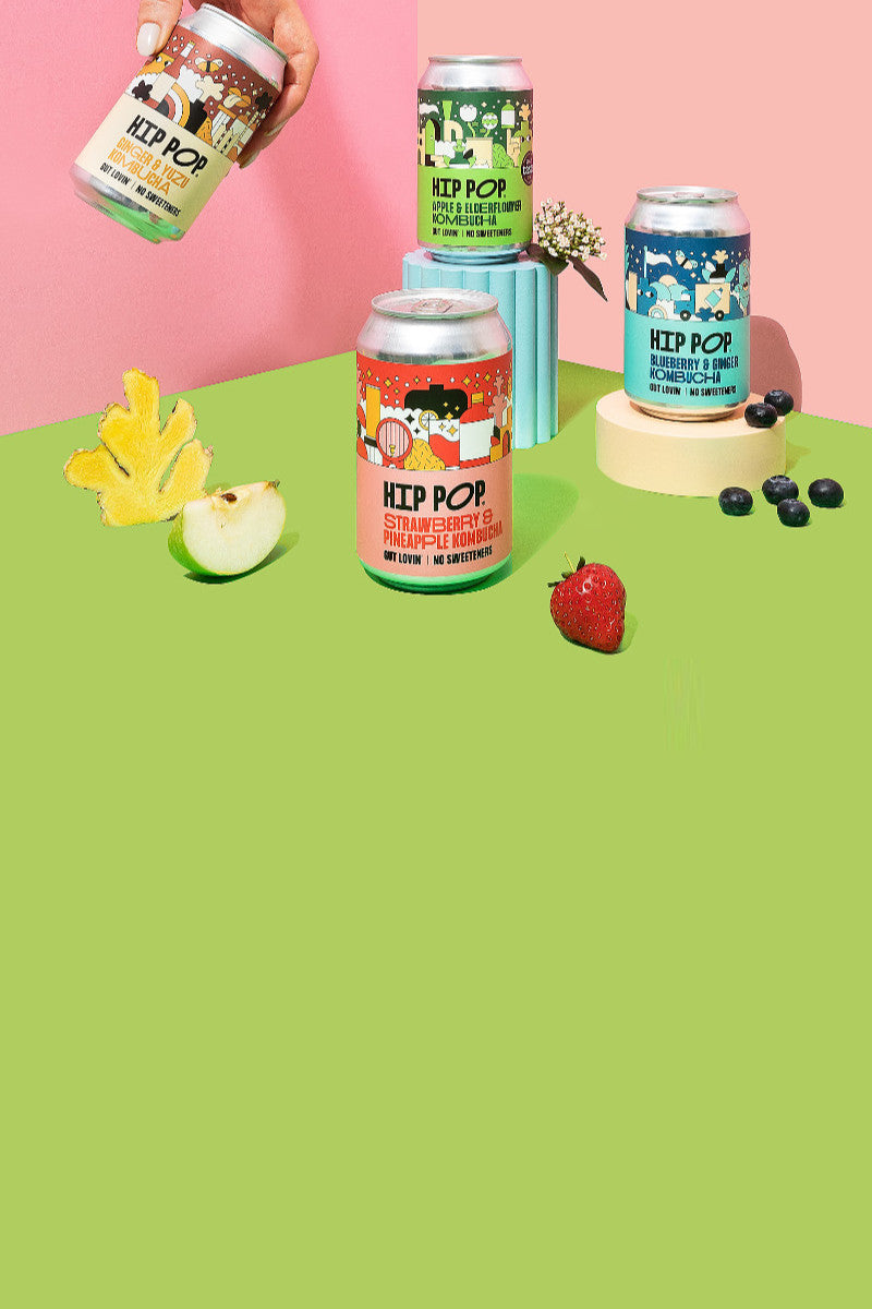 Hip Pop Kombucha collection with fruit and a hand picking up one of the cans