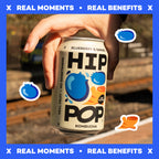 Hand holding a can of HIP Pop Kombucha with blueberry and ginger flavor, set against a blurred outdoor background and text that says "Real Moments" and "Real Benefits".