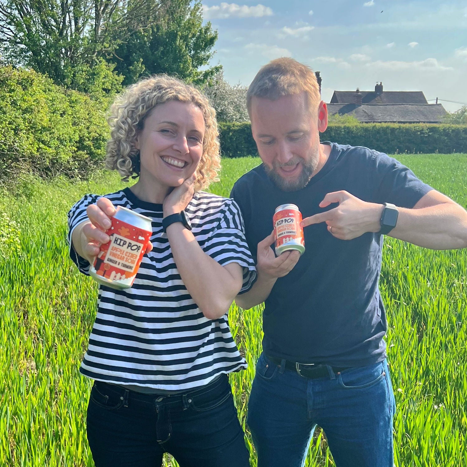 Our founders, Emma and Kenny standing in a field holding some Hip Pop living soda cans