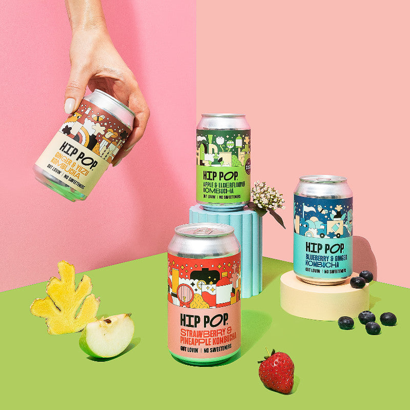 Hip Pop Kombucha collection with fruit and a hand picking up one of the cans